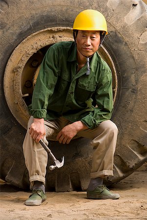 Construction worker sitting on tire of large machine Stock Photo - Premium Royalty-Free, Code: 640-01645400