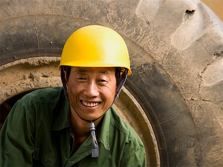 Construction worker sitting on tire of large machine smiling Stock Photo - Premium Royalty-Free, Code: 640-01645401