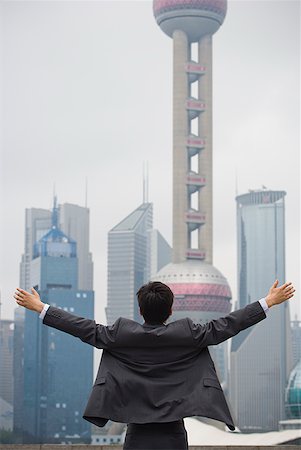 Rear view of businessman with arms up facing city skyline Stock Photo - Premium Royalty-Free, Code: 640-01645453