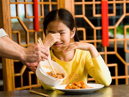 Girl sitting at table with food holding nose in disgust Stock Photo - Premium Royalty-Free, Code: 640-01645544