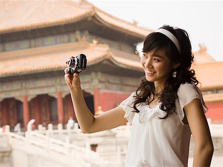 Teenage girl taking photograph outdoors with pagoda in background Stock Photo - Premium Royalty-Free, Code: 640-01645619