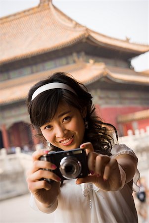 Teenage girl taking photograph outdoors with pagoda in background Stock Photo - Premium Royalty-Free, Code: 640-01645624