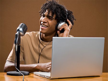 simsearch:640-02777685,k - jeune homme dans une chemise marron sur un ordinateur portable avec des écouteurs et un microphone. Photographie de stock - Premium Libres de Droits, Code: 640-02656882