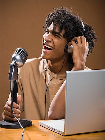 simsearch:640-02777685,k - jeune homme dans une chemise marron sur un ordinateur portable avec des écouteurs et un microphone. Photographie de stock - Premium Libres de Droits, Code: 640-02656883
