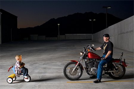 boy on a tricycle next to a man on a motorcycle Foto de stock - Sin royalties Premium, Código: 640-02658163