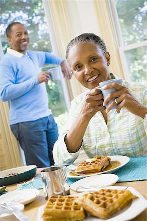 elderly black woman indoors - Portrait of a senior woman sitting at the breakfast table with a senior man standing behind her Stock Photo - Premium Royalty-Free, Code: 640-02764584