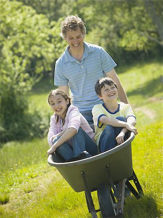 Man pushing his son and daughter in a wheelbarrow Stock Photo - Premium Royalty-Free, Code: 640-02764642