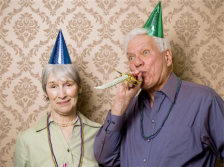 A senior man standing with a senior woman and blowing a party favor Stock Photo - Premium Royalty-Free, Code: 640-02764795