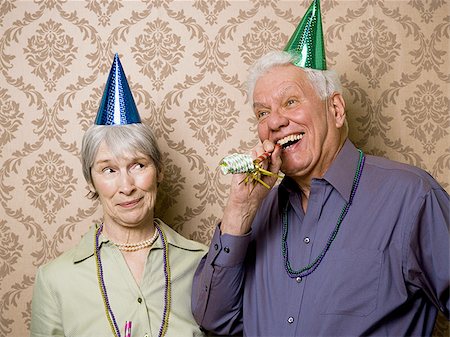 A senior man standing with a senior woman and blowing a party favor Stock Photo - Premium Royalty-Free, Code: 640-02764796
