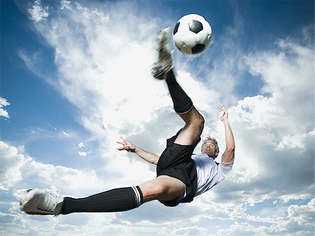 soccer player men game soccer ball kicking - Soccer player kicks ball while silhouetted against a cloudy blue sky Stock Photo - Premium Royalty-Free, Code: 640-02764961