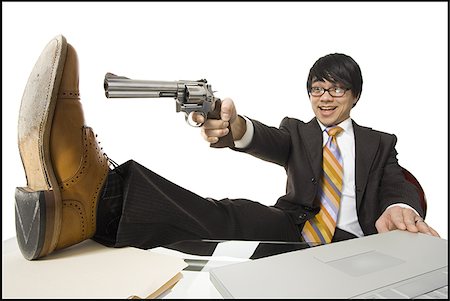 Businessman sitting at desk pointing shotgun at foot Stock Photo - Premium Royalty-Free, Code: 640-02765180