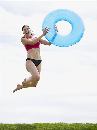 Woman in bikini jumping and smiling with swimming ring Stock Photo - Premium Royalty-Free, Code: 640-02765215