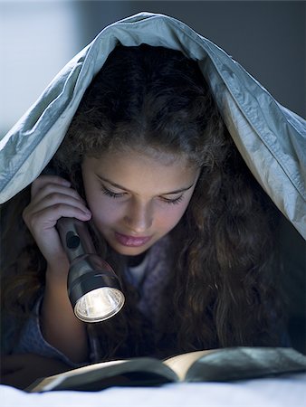 Girl laying in bed under blanket with flashlight reading Stock Photo - Premium Royalty-Free, Code: 640-02765327