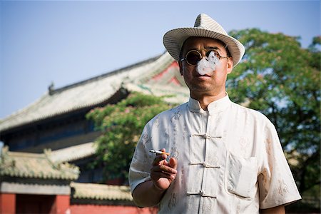 smoker - Man with sunglasses and straw hat smoking cigarette outdoors with pagoda in background Foto de stock - Sin royalties Premium, Código: 640-02765409