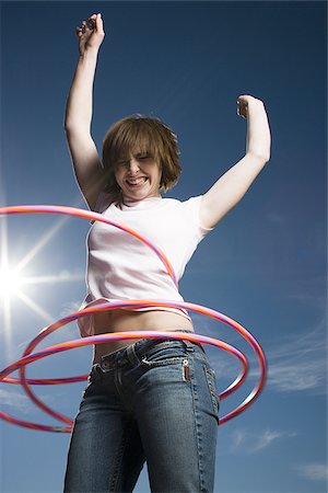 Low angle view of a teenage girl spinning hula hoops around her waist Stock Photo - Premium Royalty-Free, Code: 640-02765879