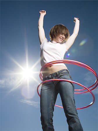 Low angle view of a teenage girl spinning hula hoops around her waist Stock Photo - Premium Royalty-Free, Code: 640-02765880