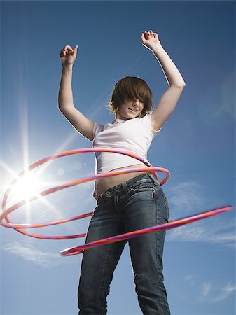 Low angle view of a teenage girl spinning hula hoops around her waist Stock Photo - Premium Royalty-Free, Code: 640-02765881