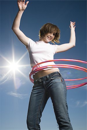 Low angle view of a teenage girl spinning hula hoops around her waist Stock Photo - Premium Royalty-Free, Code: 640-02765883