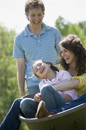 woman and her daughter sitting in a wheel barrow with a man standing beside them Stock Photo - Premium Royalty-Free, Code: 640-02767297