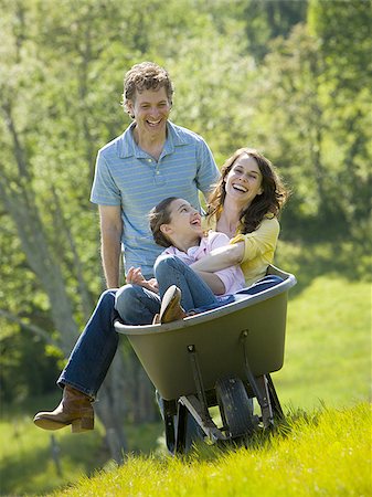 woman and her daughter sitting in a wheel barrow with a man standing beside them Stock Photo - Premium Royalty-Free, Code: 640-02767301