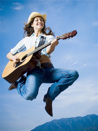 Low angle view of a young woman jumping and playing the guitar Stock Photo - Premium Royalty-Free, Code: 640-02767728