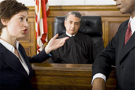 Two lawyers standing face to face in front of a male judge in a courtroom Stock Photo - Premium Royalty-Free, Code: 640-02767893