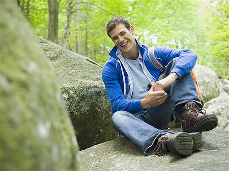 Portrait of a young man sitting in the forest and smiling Stock Photo - Premium Royalty-Free, Code: 640-02768237