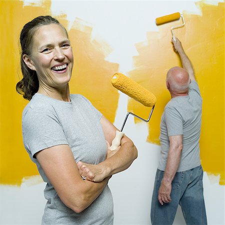 senior woman with paint roller - Portrait of a senior woman holding a paint roller with a senior man painting a wall Stock Photo - Premium Royalty-Free, Code: 640-02768329