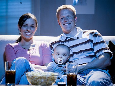 family watching tv together with popcorn - Couple on sofa with baby smiling Stock Photo - Premium Royalty-Free, Code: 640-02774044
