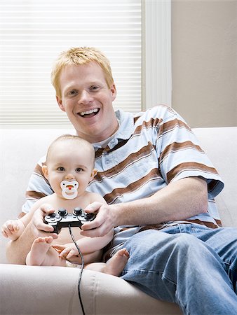 sofa two boys video game - Man and baby on sofa with video game controller smiling Stock Photo - Premium Royalty-Free, Code: 640-02774079