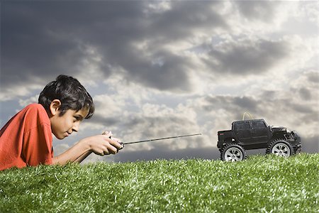 Boy playing with remote controlled truck outdoors on lawn on cloudy day Stock Photo - Premium Royalty-Free, Code: 640-02774357