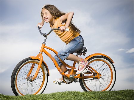 Girl sitting on orange bicycle outdoors smiling Stock Photo - Premium Royalty-Free, Code: 640-02774440