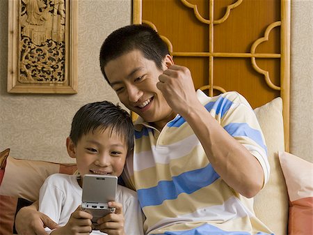 sofa two boys video game - Father and son looking at portable electronic device Stock Photo - Premium Royalty-Free, Code: 640-02775104