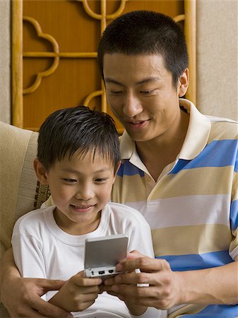 sofa two boys video game - Father and son looking at portable electronic device Stock Photo - Premium Royalty-Free, Code: 640-02775101