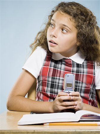 Girl sitting at desk with workbook hiding cell phone Stock Photo - Premium Royalty-Free, Code: 640-02775353