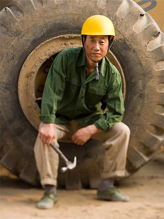 Construction worker sitting on tire of large machine Stock Photo - Premium Royalty-Free, Code: 640-02775519