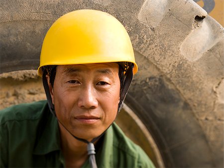 Construction worker sitting on tire of large machine smiling Stock Photo - Premium Royalty-Free, Code: 640-02775520