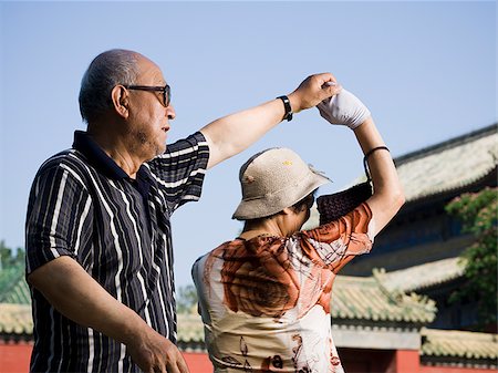 Mature couple dancing outdoors with blue sky and pagoda in background Stock Photo - Premium Royalty-Free, Code: 640-02775610