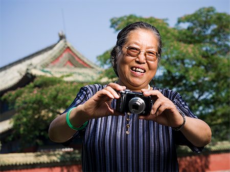 Mature woman with camera outdoors smiling Stock Photo - Premium Royalty-Free, Code: 640-02775620
