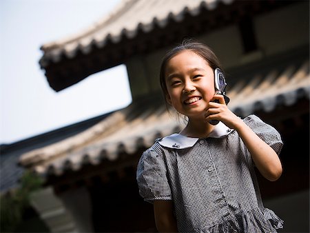 simsearch:640-02775683,k - Jeune fille debout à l'extérieur avec le téléphone cellulaire en face de la pagode souriant Photographie de stock - Premium Libres de Droits, Code: 640-02775718