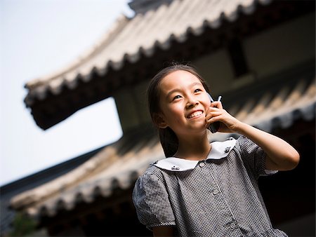 simsearch:640-02775683,k - Jeune fille debout à l'extérieur avec le téléphone cellulaire en face de la pagode souriant Photographie de stock - Premium Libres de Droits, Code: 640-02775719