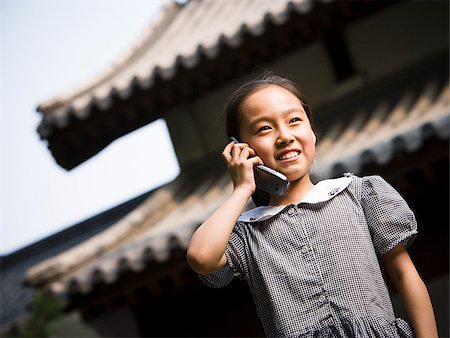 simsearch:640-02775683,k - Jeune fille debout à l'extérieur avec le téléphone cellulaire en face de la pagode souriant Photographie de stock - Premium Libres de Droits, Code: 640-02775721
