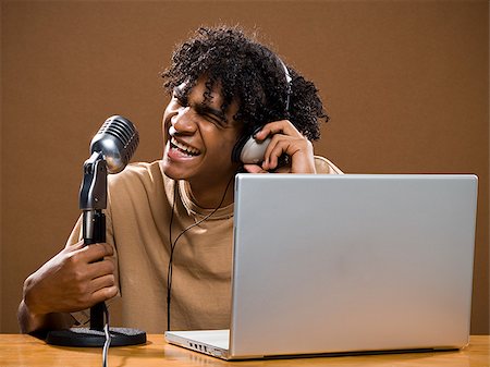 simsearch:640-02777685,k - jeune homme dans une chemise marron sur un ordinateur portable avec des écouteurs et un microphone. Photographie de stock - Premium Libres de Droits, Code: 640-02776890
