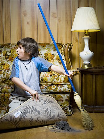 Boy sweeping dirt under rug Stock Photo - Premium Royalty-Free, Code: 640-02771085