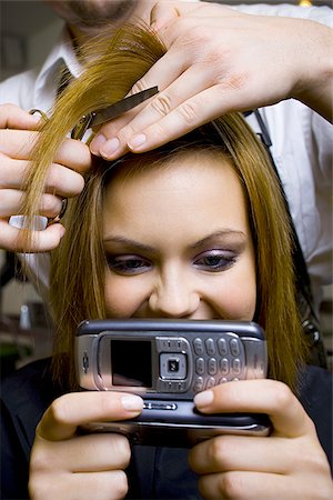 Young woman with camera phone having hair cut smiling Stock Photo - Premium Royalty-Free, Code: 640-02771544