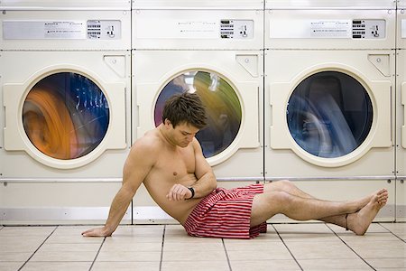 Man sitting in boxers at Laundromat checking watch Stock Photo - Premium Royalty-Free, Code: 640-02771649