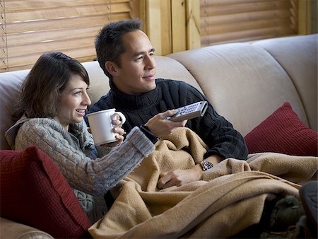 Mann und Frau auf Sofa mit Tassen und Fernbedienung Stockbilder - Premium RF Lizenzfrei, Bildnummer: 640-02771966