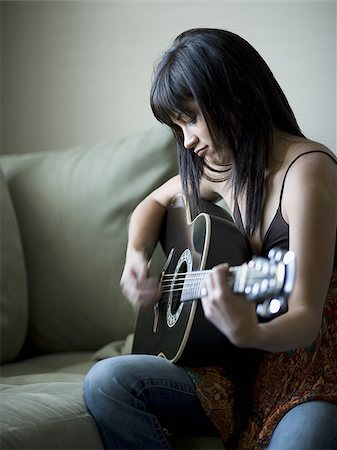 Woman sitting on sofa with laptop and headphones playing guitar Stock Photo - Premium Royalty-Free, Code: 640-02772787