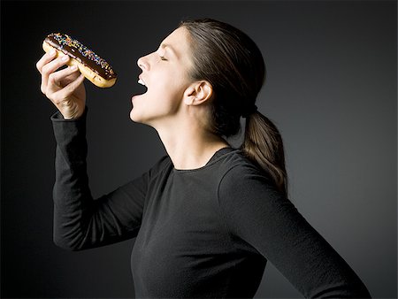 Profile of woman eating an Éclair donut Stock Photo - Premium Royalty-Free, Code: 640-02773838
