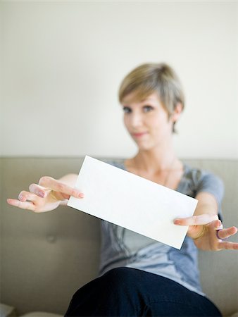 woman sitting on a couch holding up an envelope Stock Photo - Premium Royalty-Free, Code: 640-02950154